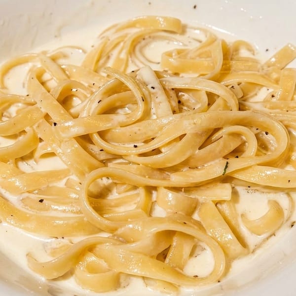 Creamy fettuccine alfredo with cracked black pepper in a white bowl.